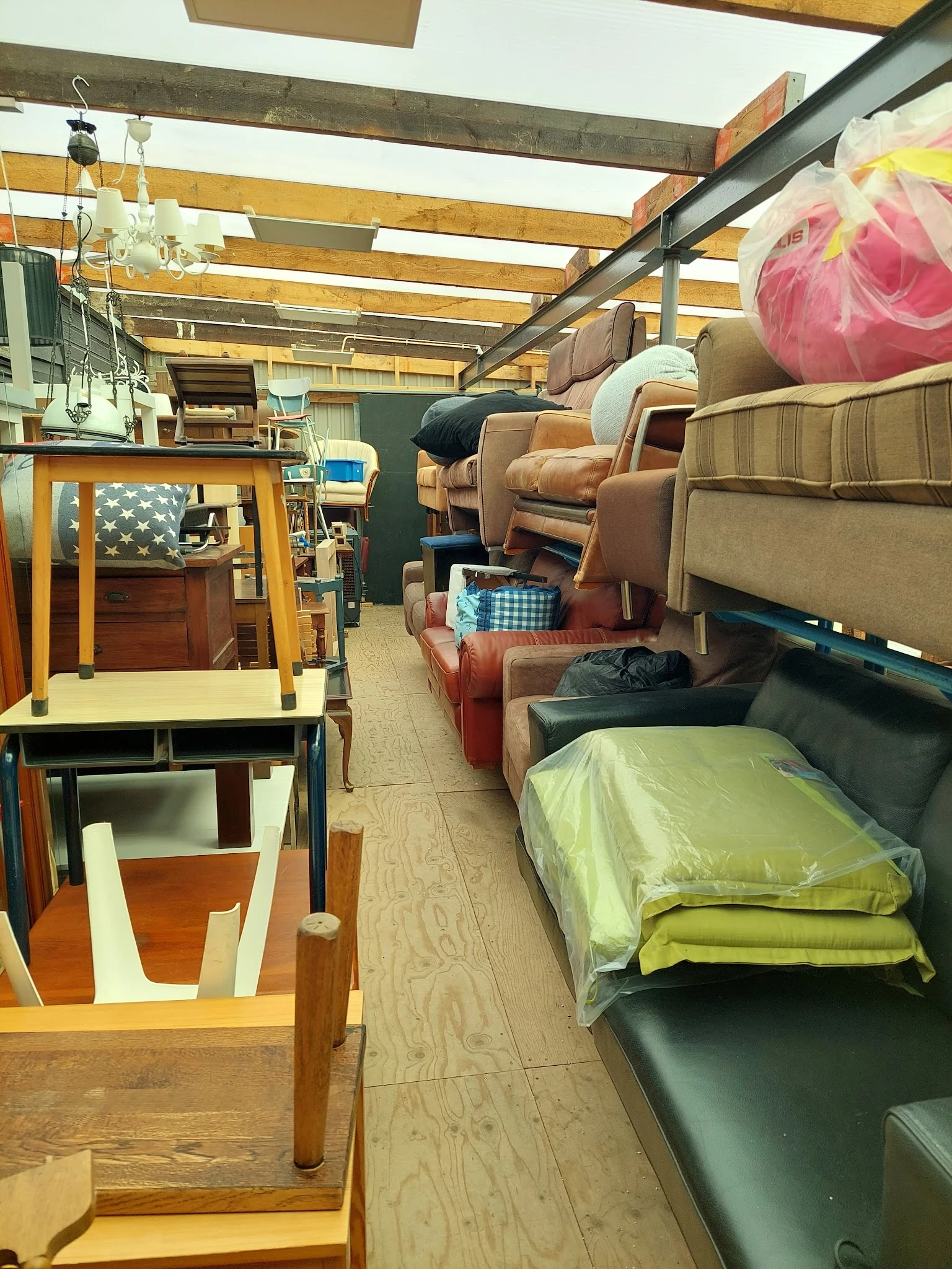 Kringloopwinkelinterieur met meubels, stoelen, bedden en huishoudelijke artikelen langs het gangpad