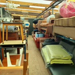 Kringloopwinkelinterieur met meubels, stoelen, bedden en huishoudelijke artikelen langs het gangpad