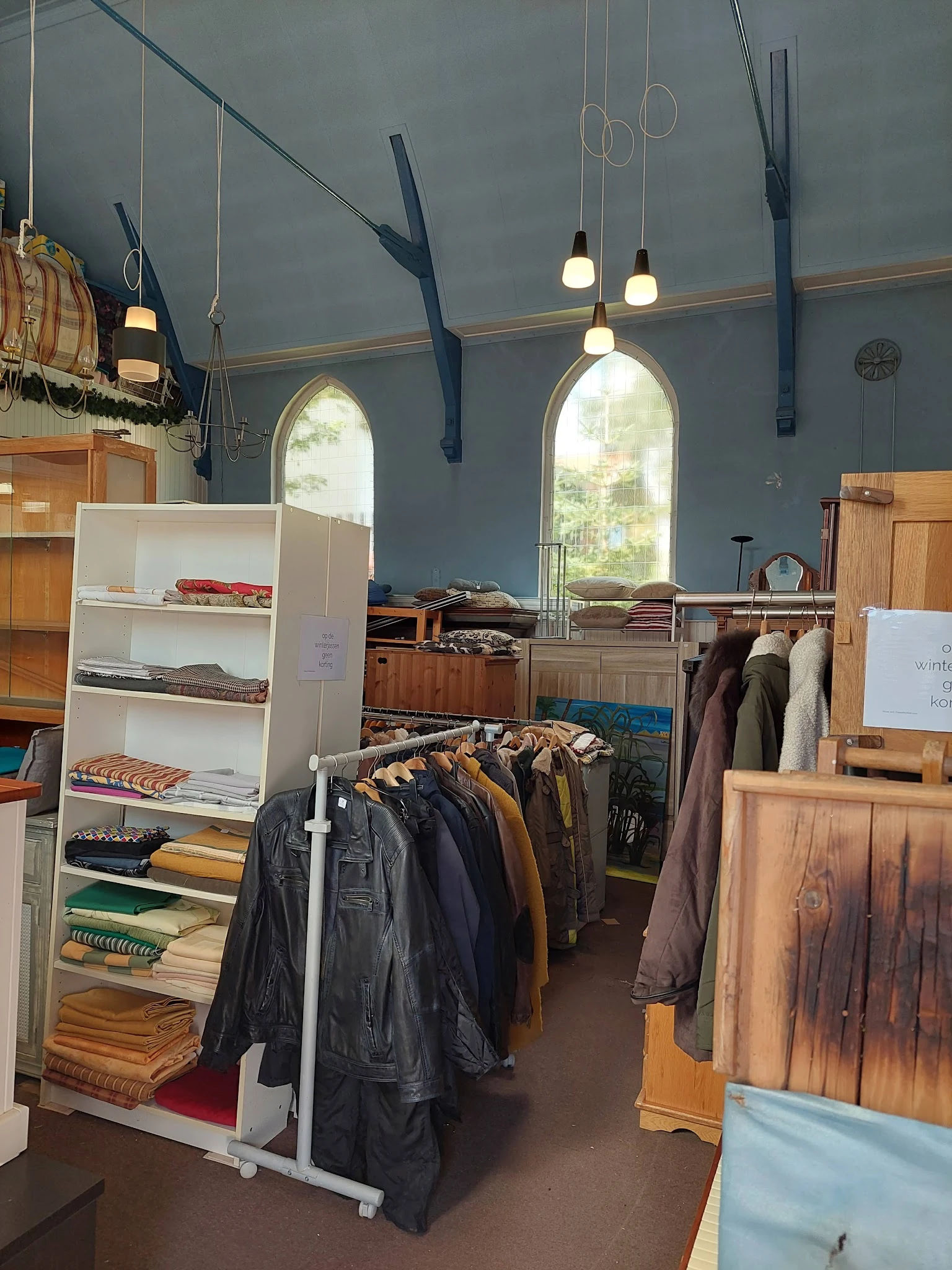 Winkelbinnenruimte met kledingrekken, stellingen met textiel en hoge ramen met natuurlicht