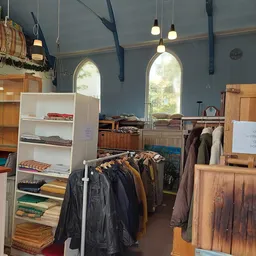 Winkelbinnenruimte met kledingrekken, stellingen met textiel en hoge ramen met natuurlicht