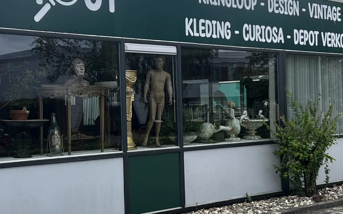 Winkelgevel met groene deur, witte en donkergroene pui, etalageruiten met beeldhouwerken en decoratieve objecten