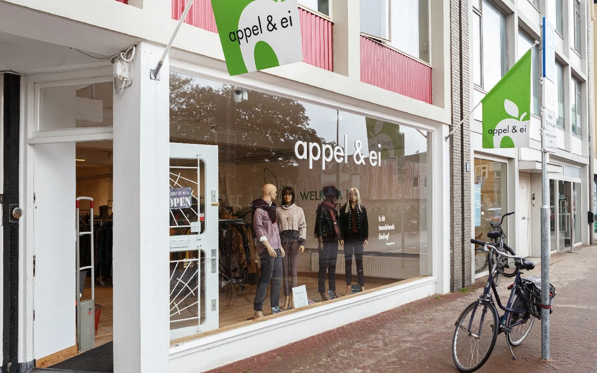 Winkelpui van kledingwinkel met grote glazen raam, mannequins in de etalage en groene logo's boven