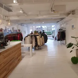 Heldere winkelruimte met kledingrekken, houten balie en decoratieve hangende lampen