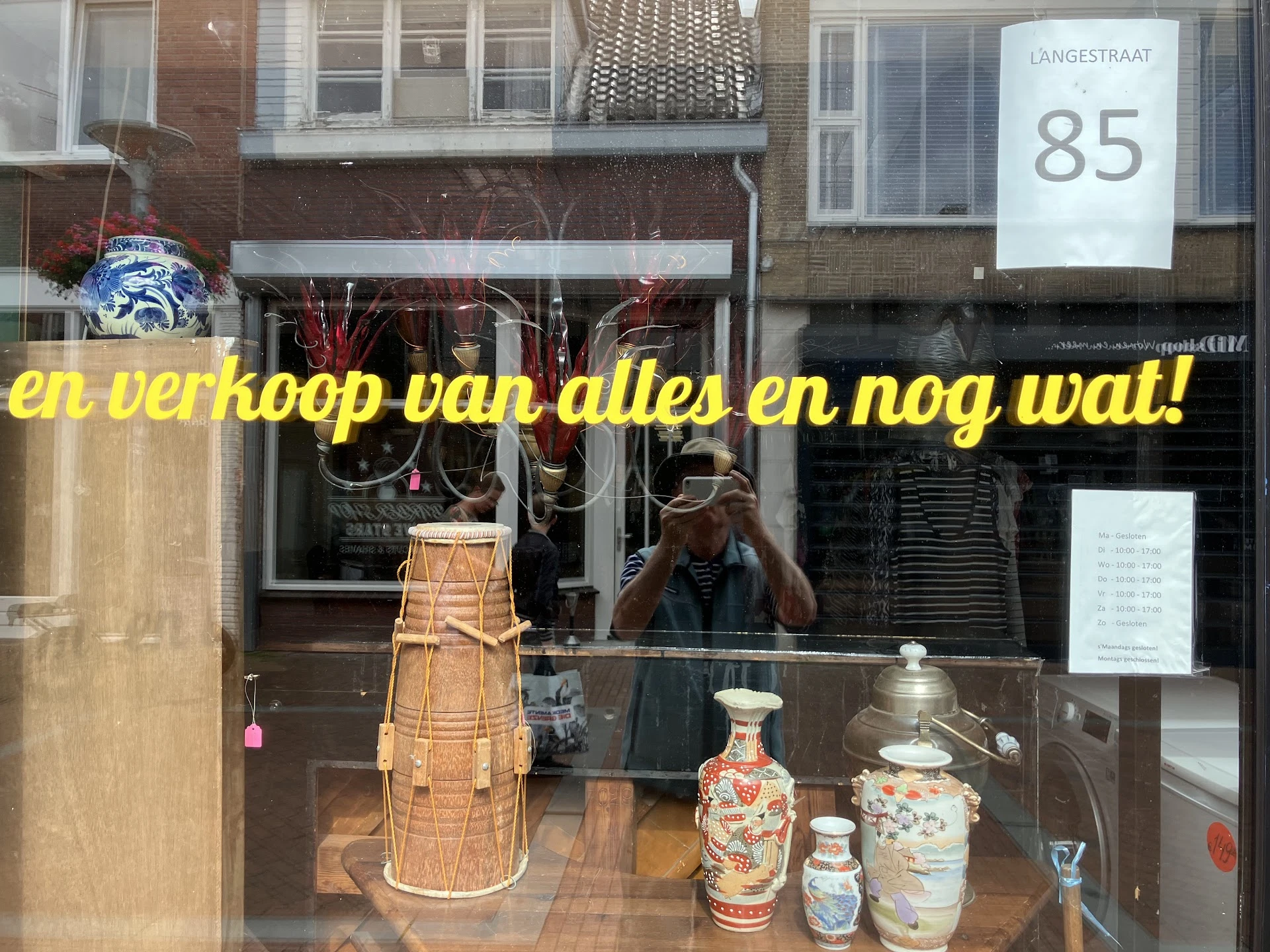 Etalage met diverse secondhandspullen: rieten mand, decoratieve vazen en servies.