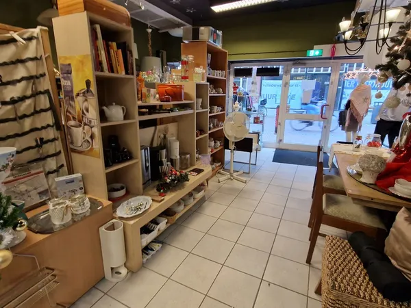 Winkelvloer van kringloopwinkel met houten stellingkasten, uitgestalde spullen en zicht op de ingang