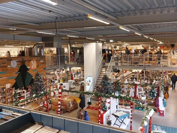 Overzicht van de kringloopwinkel met meerdere verdiepingen, tafels met kerstdecoraties en spullen, stellingen met artikelen e