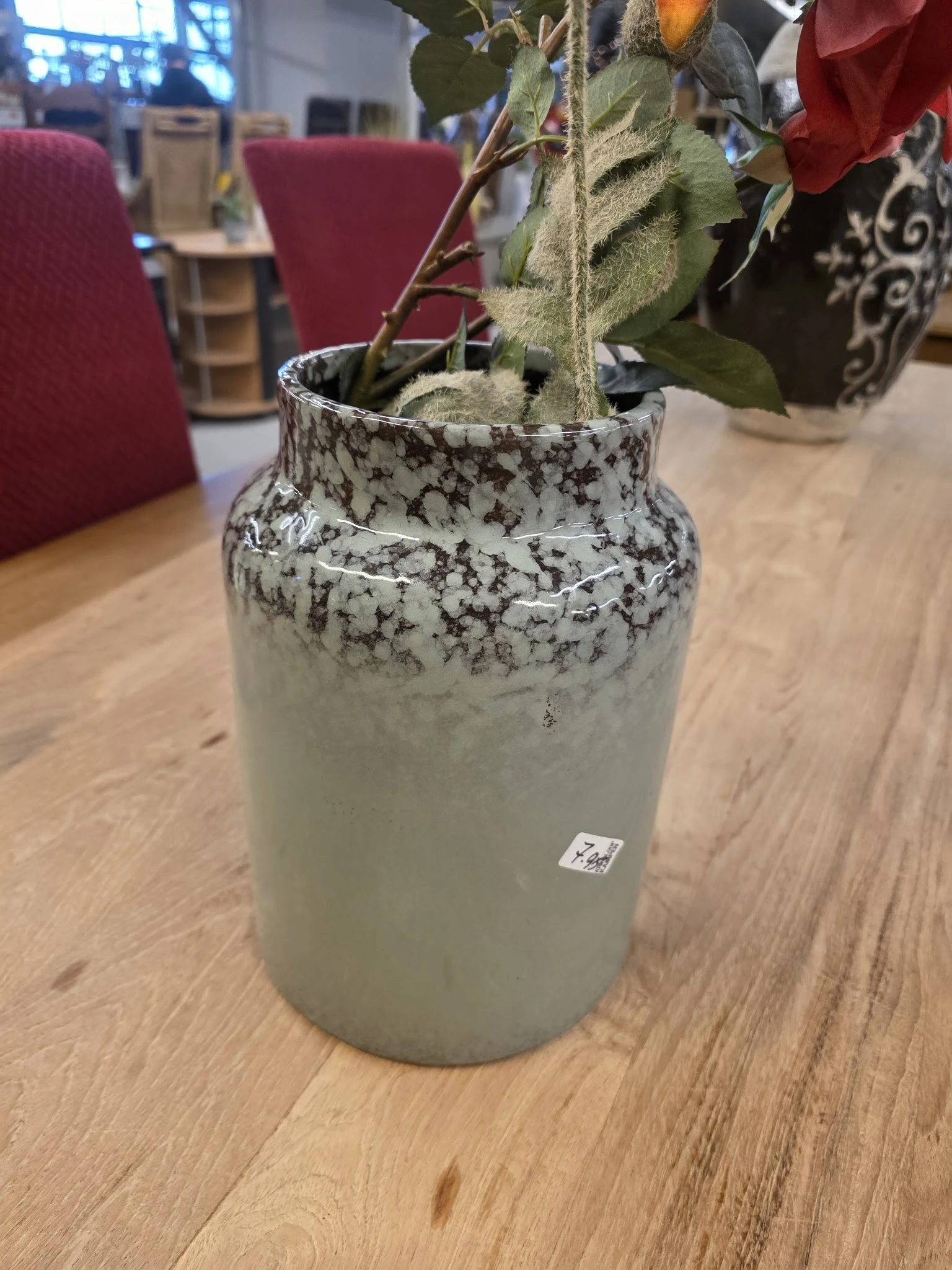 Grijswitte keramische vaas met versiering, gevuld met droogbloemen en takken op houten tafel