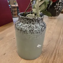 Grijswitte keramische vaas met versiering, gevuld met droogbloemen en takken op houten tafel