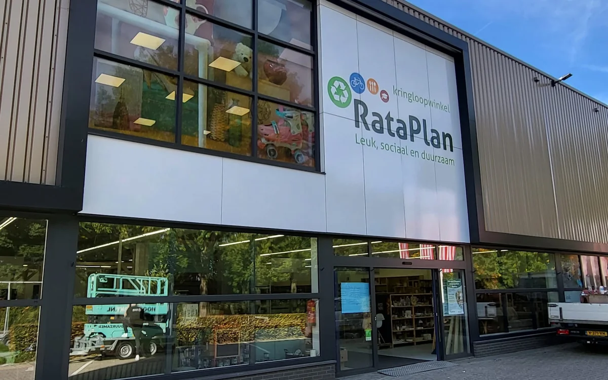 Moderne gevel van Kringloop RataPlan met grote ramen, ingang en grijze golfplaten wanden