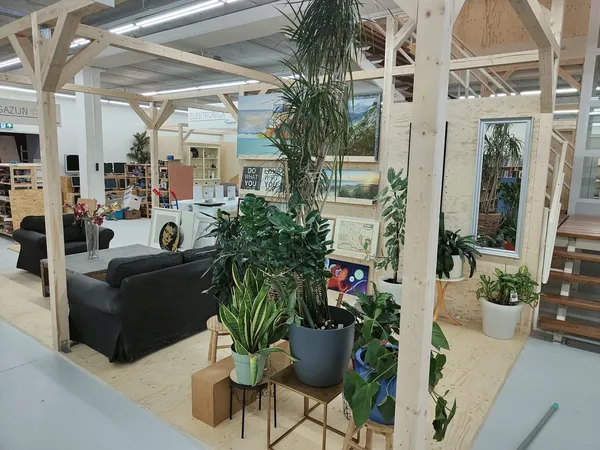 Winkelinterieur met houten balkenstructuur, potplanten op verschillende niveaus, zwarte bank op achtergrond en displays met p