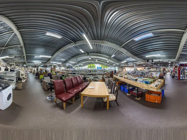 Ruim winkelinterieur van kringloopwinkel met gestoffeerde zitmeubels, houten tafels, diverse stellingen met spullen en een wi