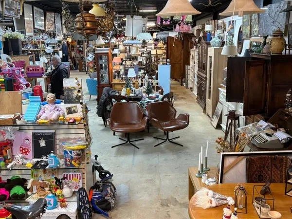 Overzicht van kringloopwinkel met vintage meubels, lampen, decoratie en diverse tweedehands artikelen op de vloer