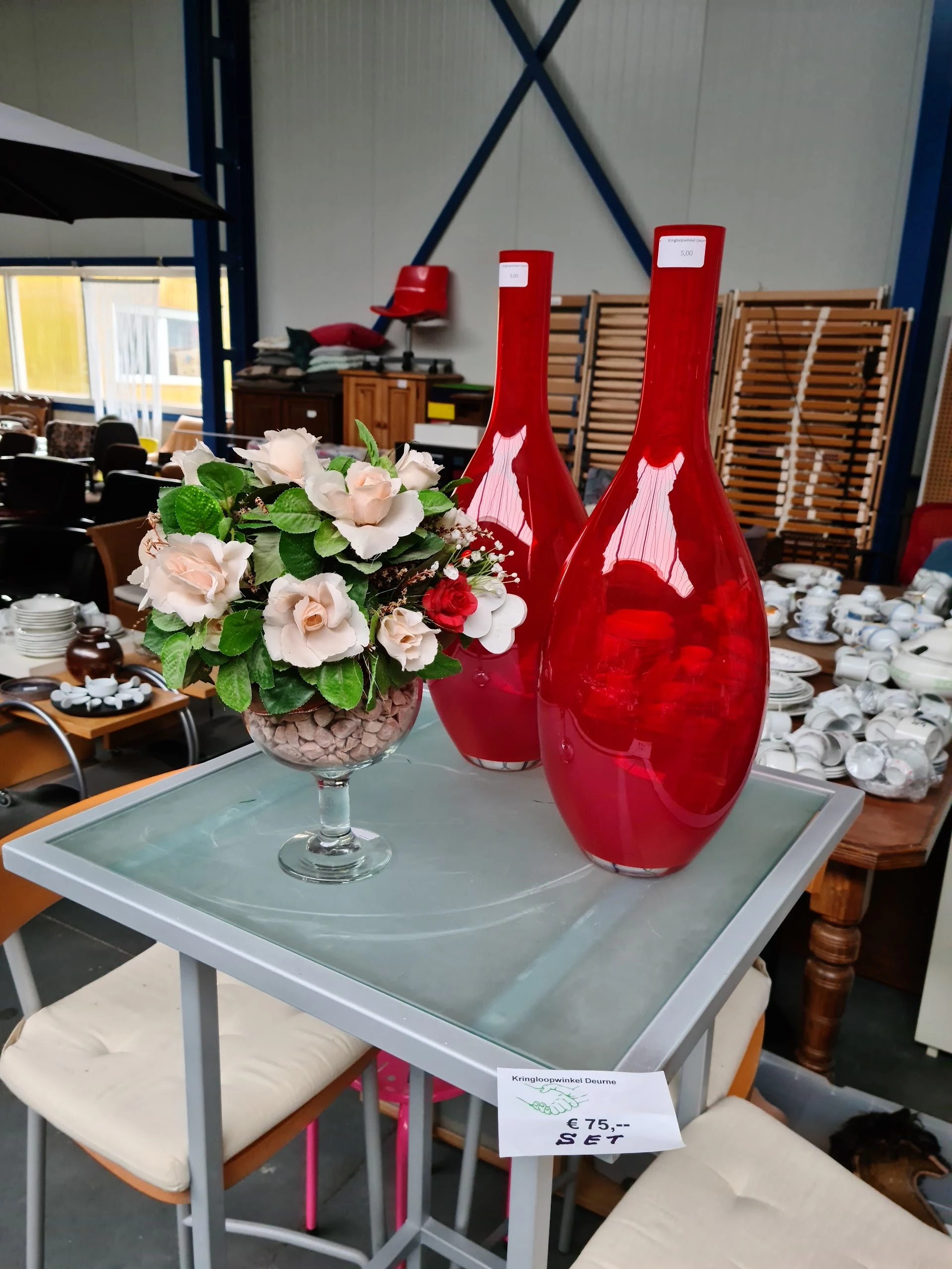 Glazen vaas met roze en rode kunstbloemen en twee rode decoratieve flessen op een grijze tafel