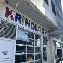 Gevel van kringloopwinkel Kringloop met gekleurde letters op witte gevel, grote ramen en adres 1852