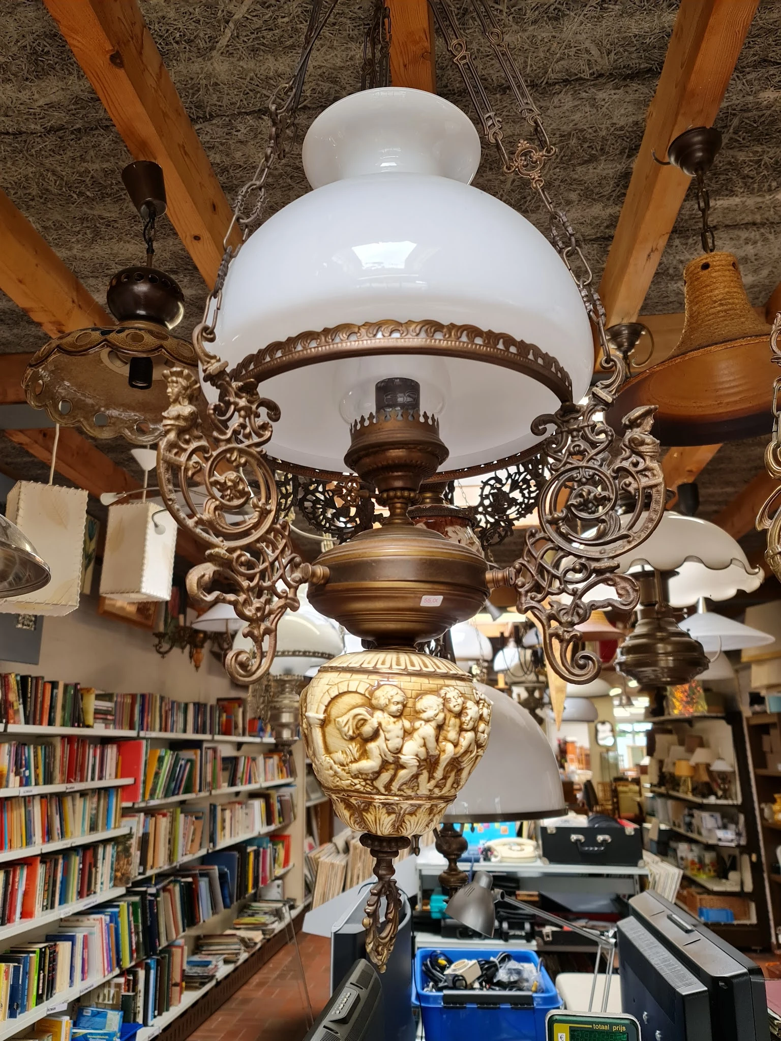 Antieke hanglamp met wit glazen kap en ornamentaal bronzen beugels, opgehangen in de winkel