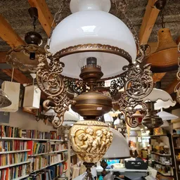 Antieke hanglamp met wit glazen kap en ornamentaal bronzen beugels, opgehangen in de winkel