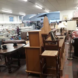 Winkelvloer met tweedehands meubels: tafels, stoelen, kasten en een roze bank; op de achtergrond stellingen met spullen