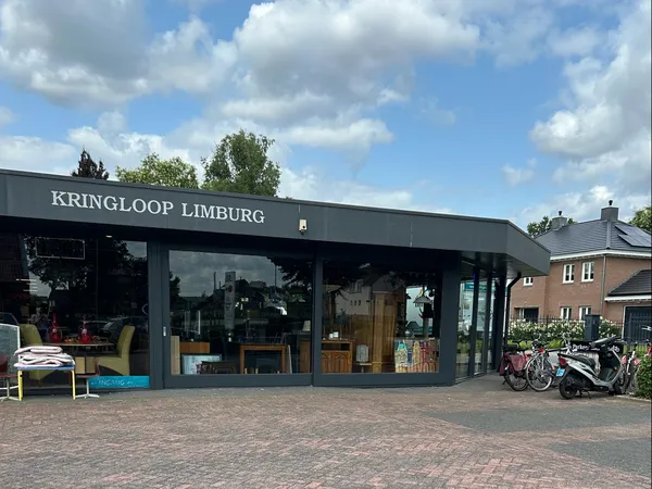 Voorgevel van kringloopwinkel met grote ramen, donkergroene pui en winkelnaam KRINGLOOP LIMBURG, fietsen en spullen zichtbaar