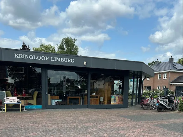 Gevel van kringloopwinkel met grote ramen, zwarte pui en zichtbare winkelinventaris, fietsen buiten geparkeerd