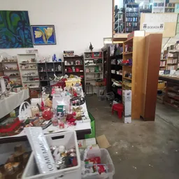 Binnenzicht van kringloopwinkel met tafels vol spullen, stellingen en dozen verspreid over de winkelvloer