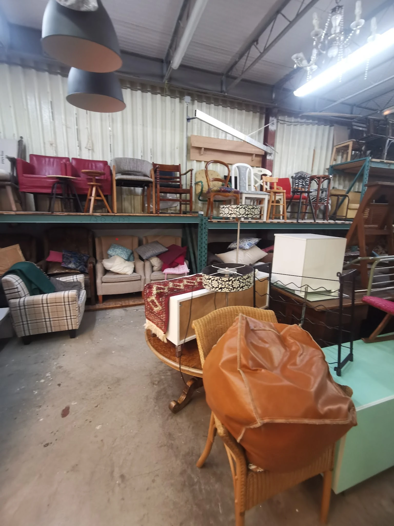Magazijnruimte vol tweedehands meubilair: stoelen, bedden, kasten en andere meubels op verschillende niveaus opgesteld