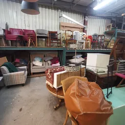 Magazijnruimte vol tweedehands meubilair: stoelen, bedden, kasten en andere meubels op verschillende niveaus opgesteld