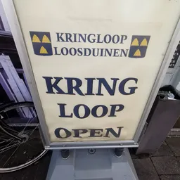 Wit A-bord met donkerblauwe tekst 'KRING LOOP OPEN' en logo van Kringloop Loosduinen op straat