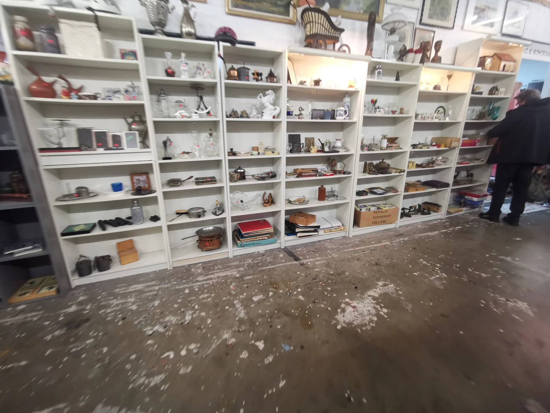 Witte stellingen tegen de wand gevuld met diverse huishoudelijke spullen en decoratie-artikelen in een kringloopwinkel