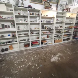 Witte stellingen tegen de wand gevuld met diverse huishoudelijke spullen en decoratie-artikelen in een kringloopwinkel