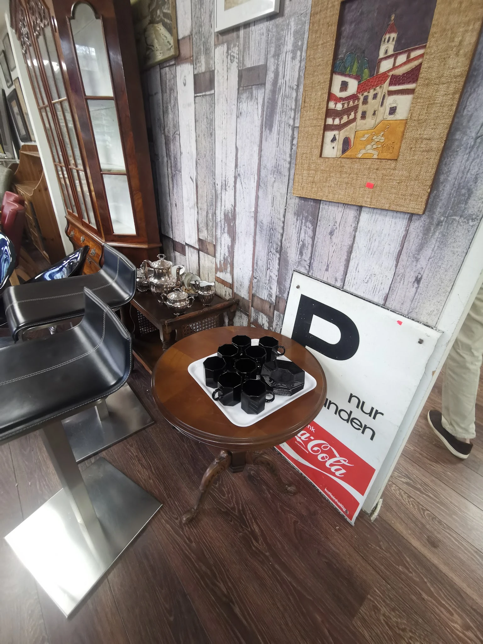 Bruine ronde tafel met zwarte handschoenen, naast een Coca-Cola bord en andere winkelspeullen