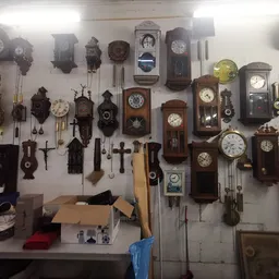 Muur vol met diverse antieke en vintage wandklokken in verschillende stijlen en formaten