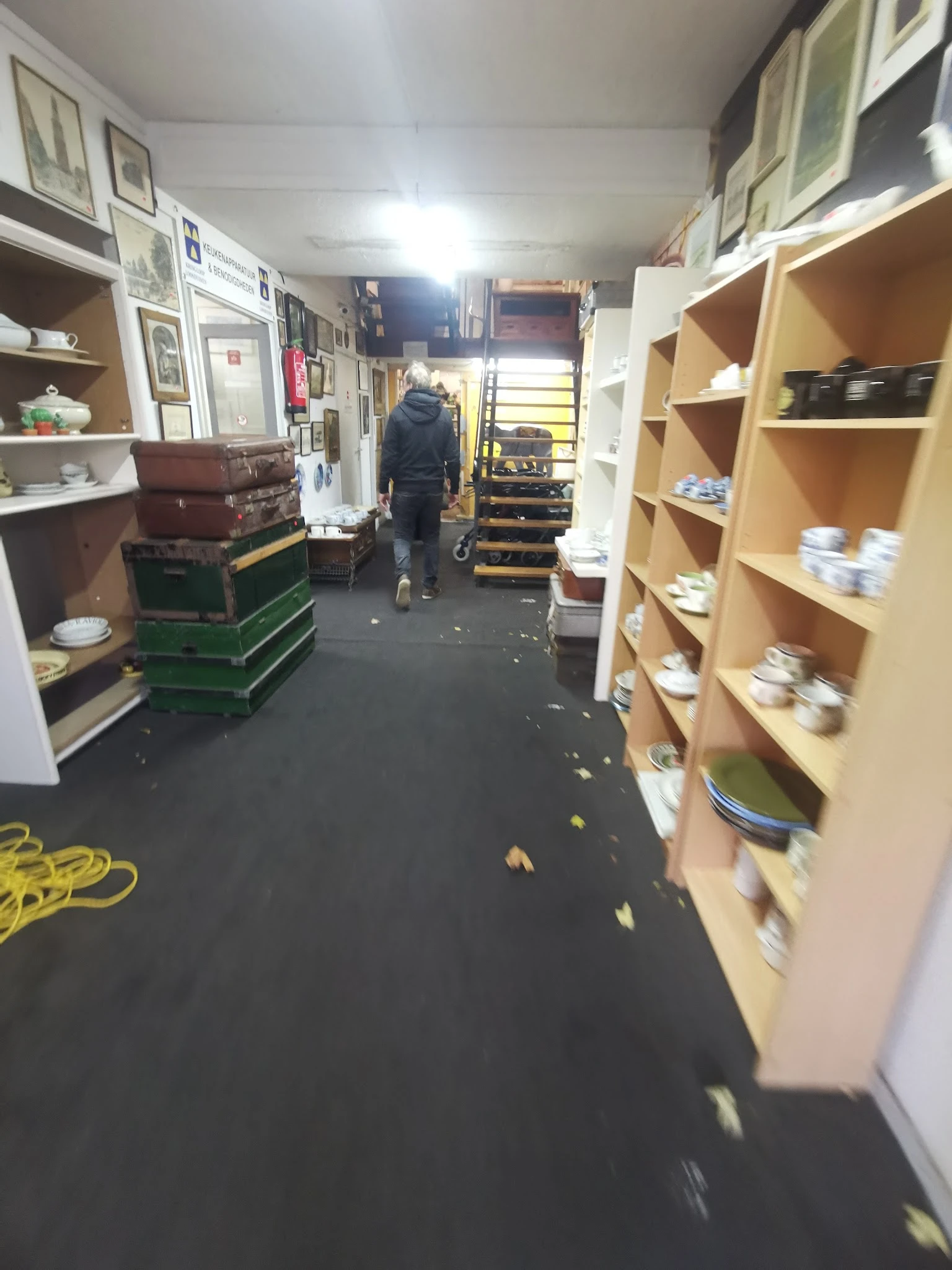 Winkelinterieur met houten stellingen vol potten en bakken, groene en rode kratten op de vloer, en een medewerker in het acht