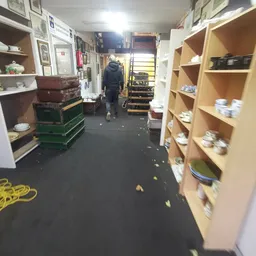 Winkelinterieur met houten stellingen vol potten en bakken, groene en rode kratten op de vloer, en een medewerker in het acht