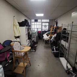 Rommelige opslagruimte of werkplaats met muziekinstrumenten, stoelen, kleding en diverse spullen