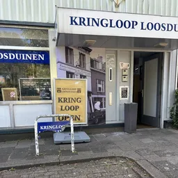 Winkelpui van kringloopwinkel met gele en blauwe borden, deur en ramen aan straat