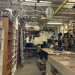 Binnenzicht van kringloopwinkel met stellingen boeken aan linkerkant, werkplekken met computers en instrumenten in het midden