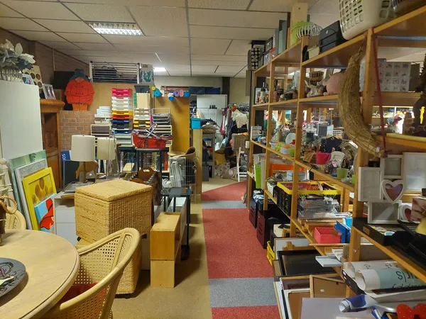 Winkelinterieur met houten stellingen, diverse spullen, rode lopers en gekleurde wanden