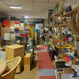 Overzicht van de winkelvloer met houten stellingen, meubelstukken en diverse spullen langs rode looppad