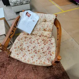 Houten fauteuil met beige/roze bloemenpatroon en een instructiepapier op de zitting