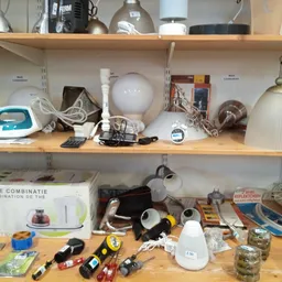 Stellingen met diverse huishoudelijke artikelen zoals lampen, strijkijzer, speakers en keukengerei