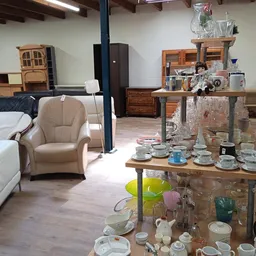 Ruime kringloopwinkel met meubels, serviesgoed en huishoudelijke spullen uitgestald op tafels en kasten