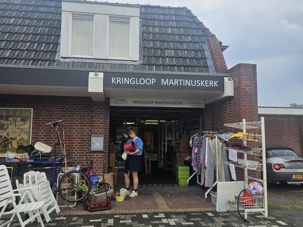 Voorgevel van kringloopwinkel Martinuskerk met opengaande deur, uithangbord en diverse tweedehands spullen op straat