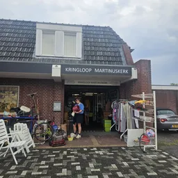 Voorgevel van kringloopwinkel Martinuskerk met opengaande deur, uithangbord en diverse tweedehands spullen op straat