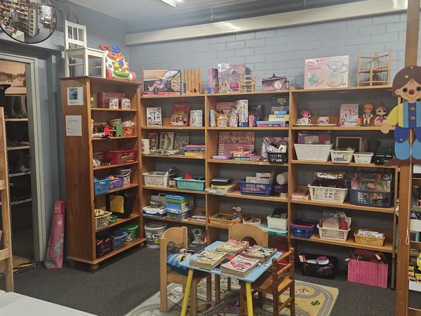Winkelvloer met houten boekenkast en stellingen vol speelgoed, boeken en diverse gebruiksartikelen