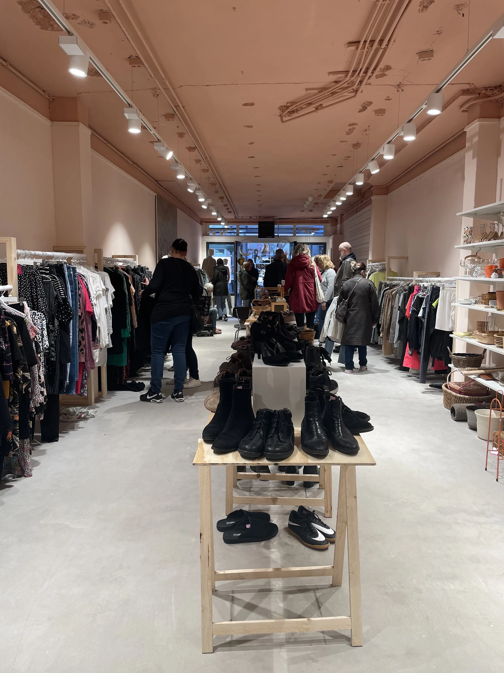 Winkelvloer met kledingrekken, bezoekers en een display met schoenen in het midden
