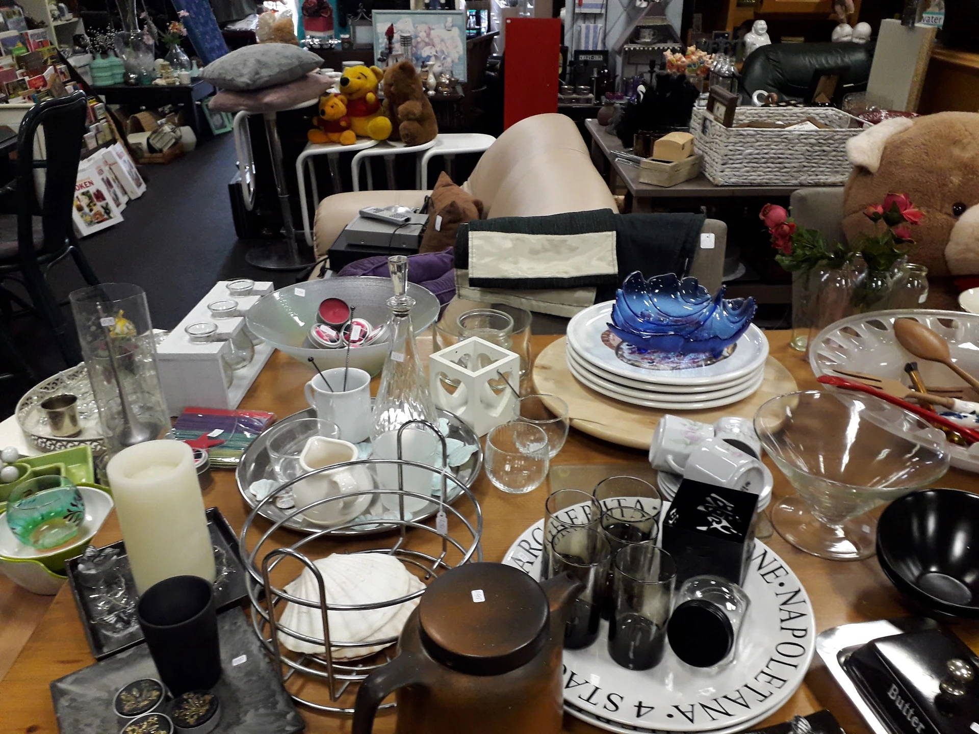 Tafel vol huishoudelijke artikelen: servies, glazen, kaarshouders en decoratieve items in een winkel