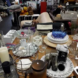 Tafel vol huishoudelijke artikelen: servies, glazen, kaarshouders en decoratieve items in een winkel