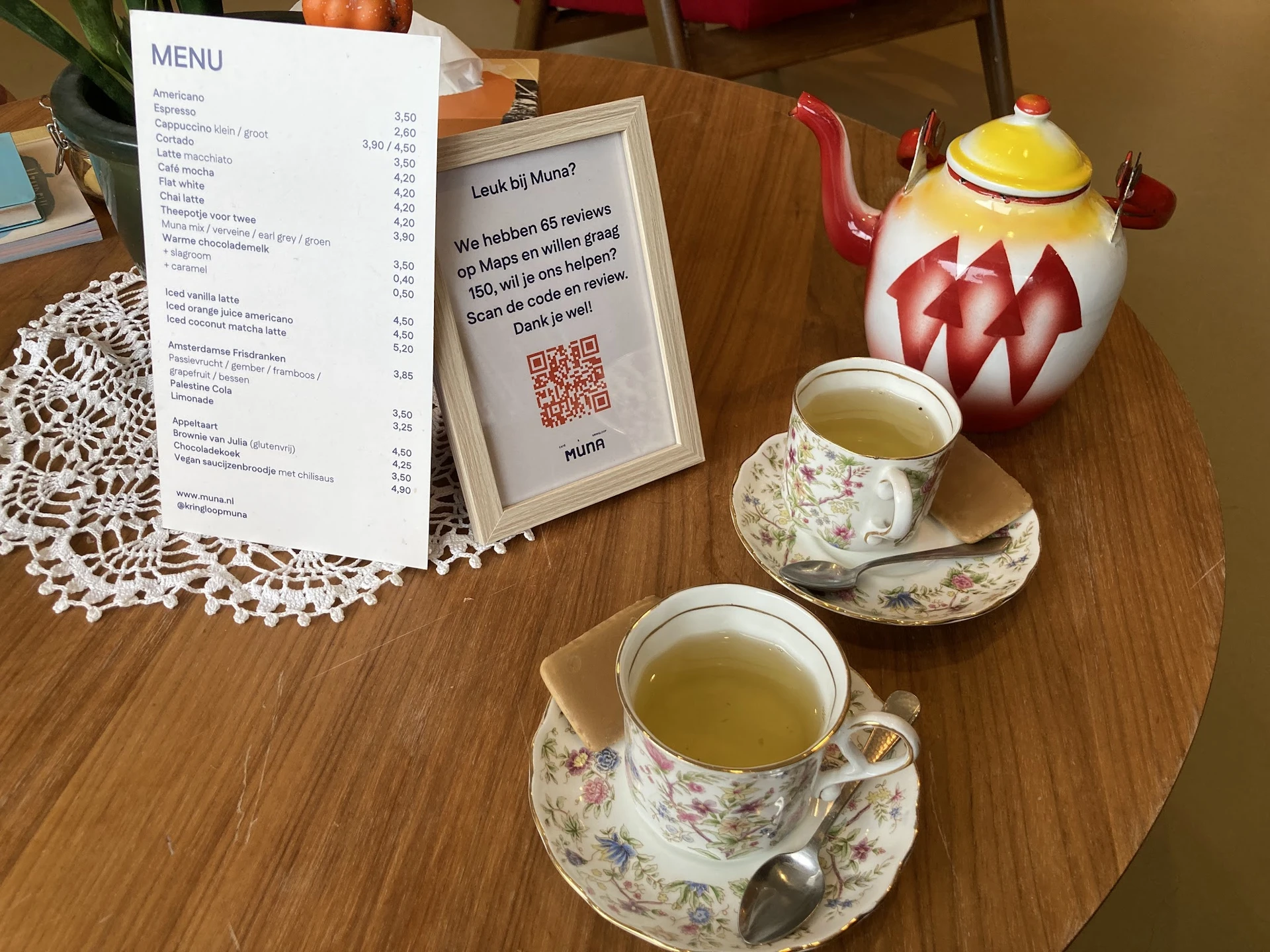 Twee kopjes thee op bloemmotief schotels met een menukaart en decoratieve theepot op tafel