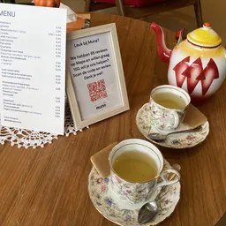 Twee kopjes thee op bloemmotief schotels met een menukaart en decoratieve theepot op tafel