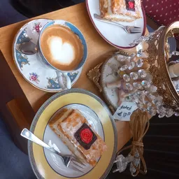 Kopje cappuccino met latte art en gebakje met rode roosdecoratie op decoratieve borden